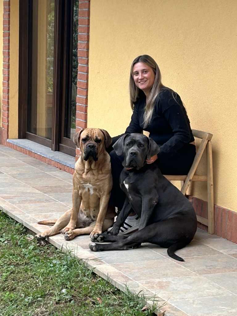 Donna seduta sul portico con due cani grandi accanto a una parete gialla.